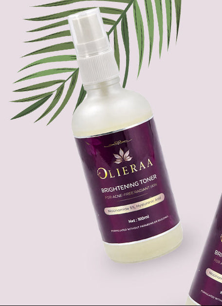 Two bottles of Olieraa hair care product on a light pink background with green leaves.